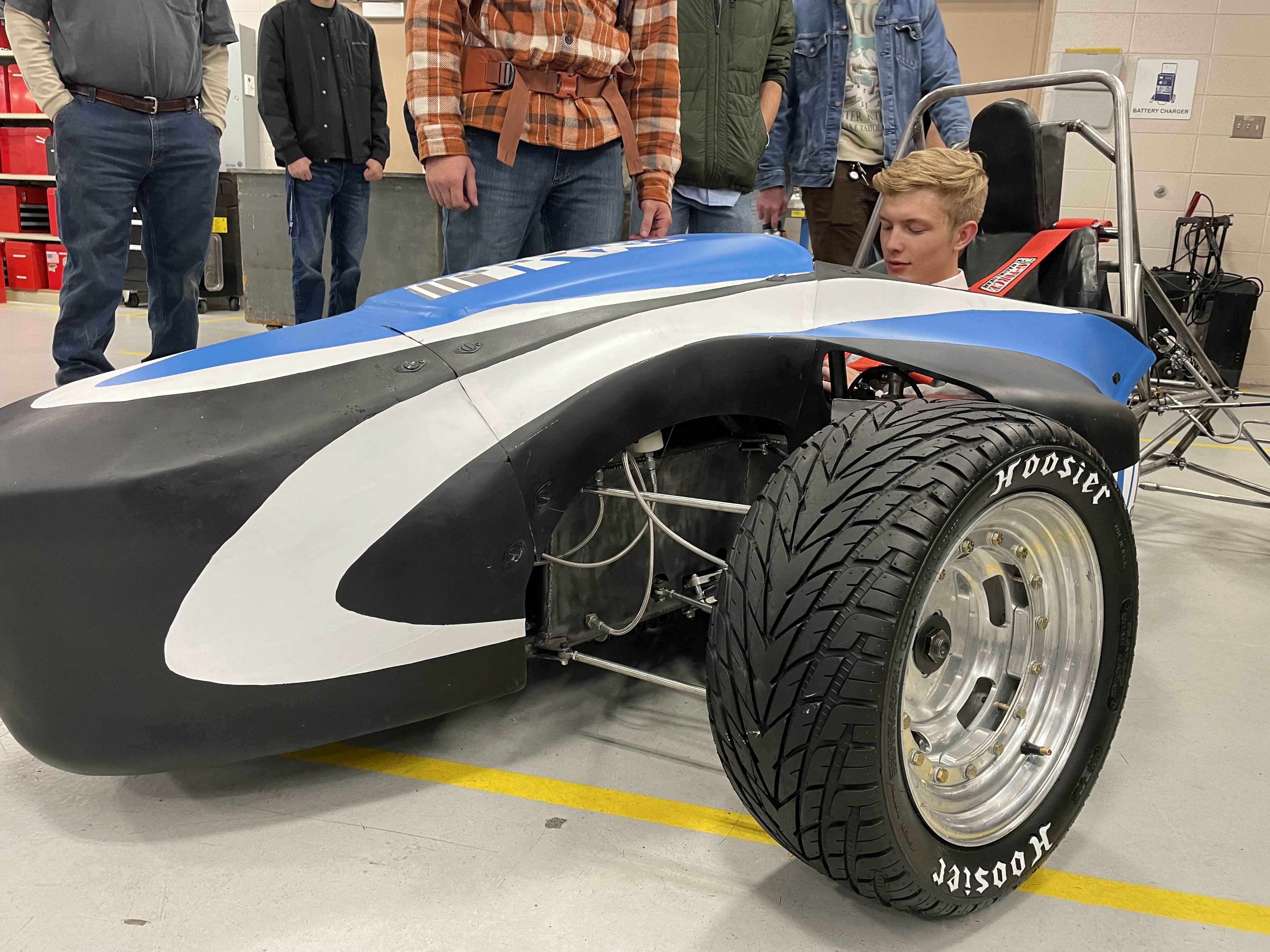 A team member seated in the blue, white, and black formula car in the workshop