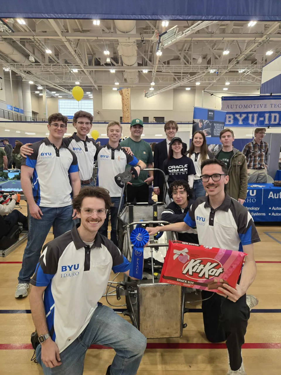 BYU-I Formula Racing team members gathered around a car chassis at an indoor event